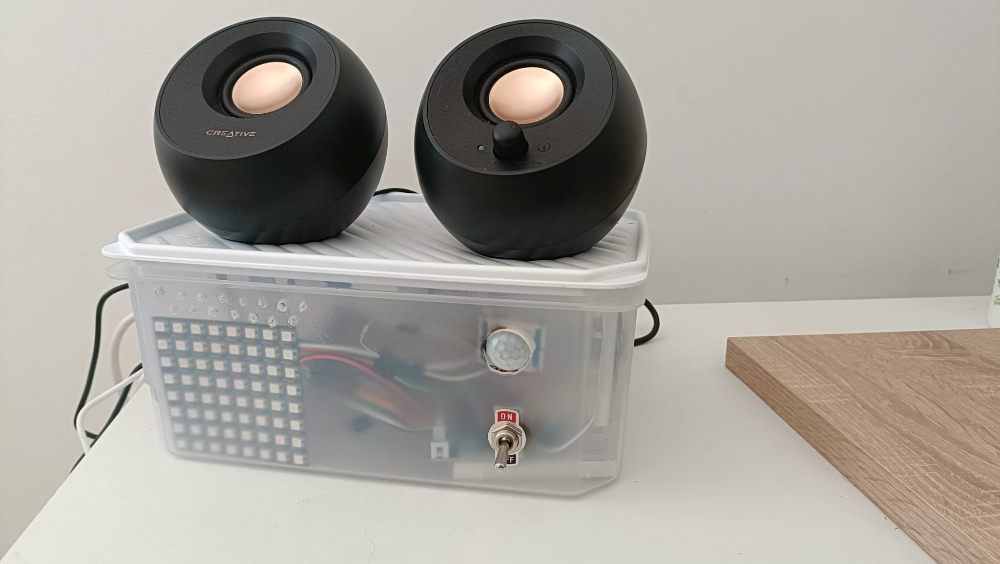 El prototipo real del asistente: una caja transparente con matriz de LEDs, sensor de presencia e interruptor físico, con los altavoces encima, en su sitio de pruebas.